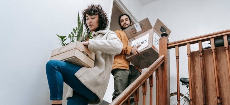 Couple Going Down The Stairs With Box Of Books And Plants