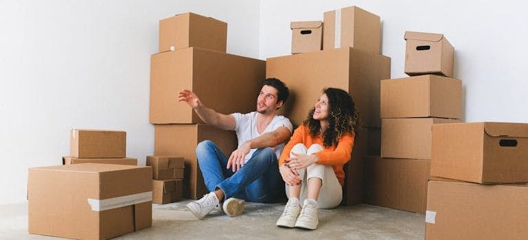 Man and Woman Sitting on Floor Beside Pile of Boxes