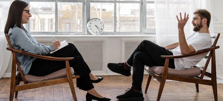 Person in Black Pants and Black Shoes Sitting on Brown Wooden Chair