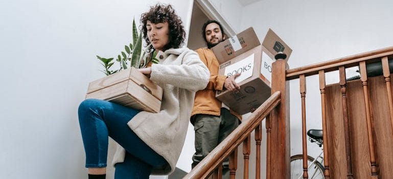 Couple Going Down The Stairs With Box Of Books And Plants