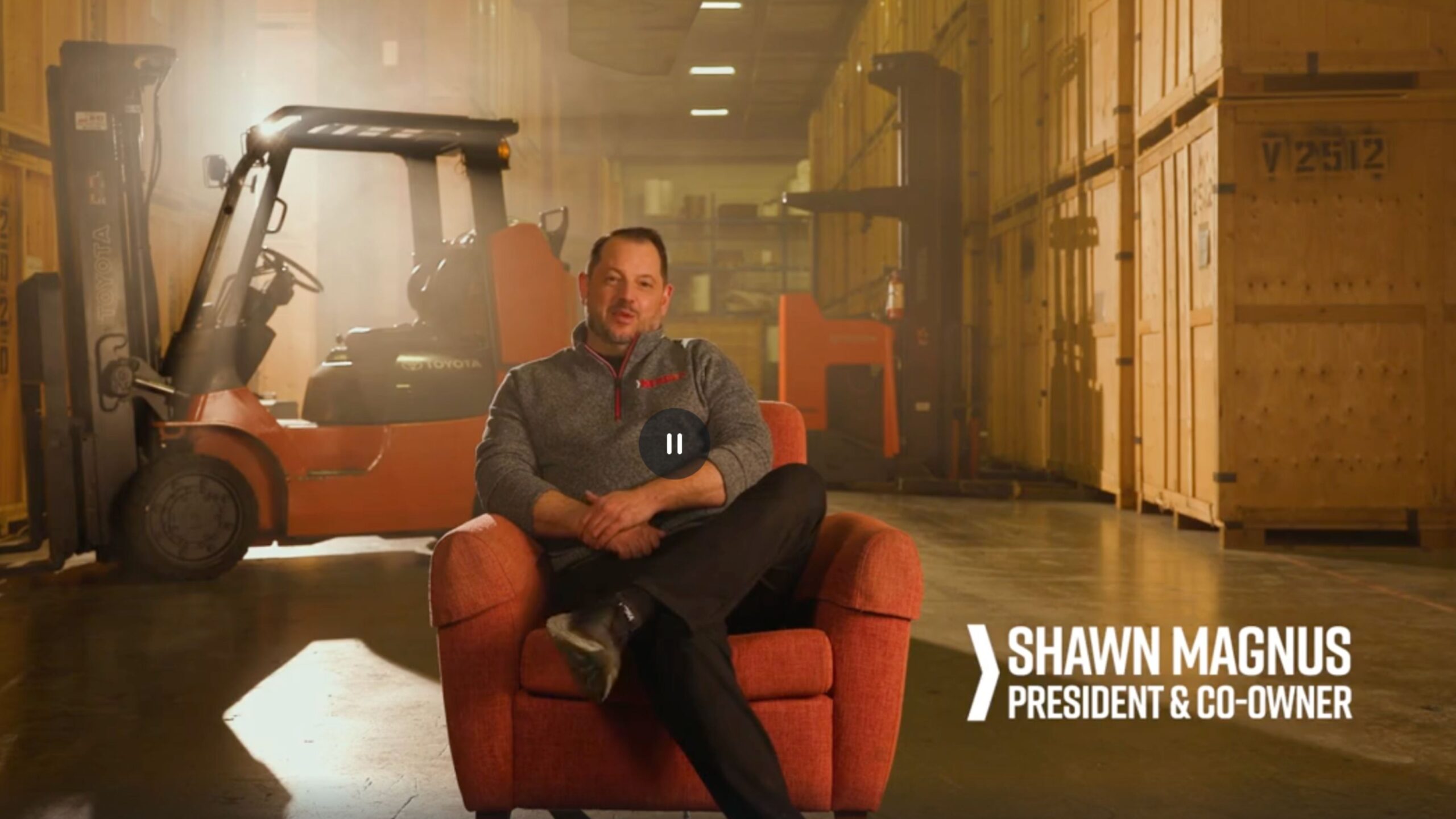 Shawn sitting in an armchair in the Hendra storage warehouse, with crates and forklift in the background.